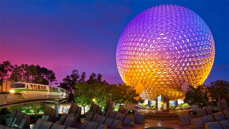 a monorail going by a large dimpled ball-shaped structure