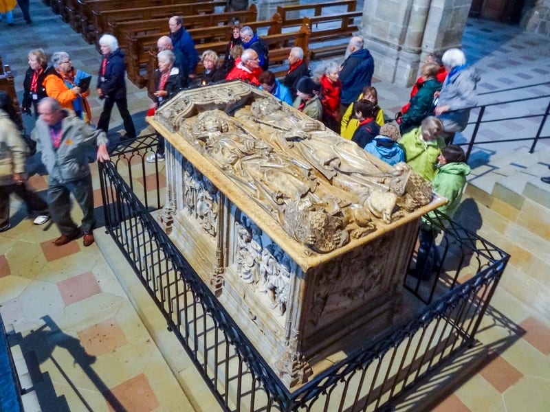 people walking past an ornately carved tomb in a church