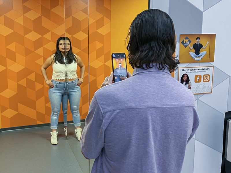 a man photographing a woman near a large mirror in a museum - one of the Things to Do in Orlando for Adults