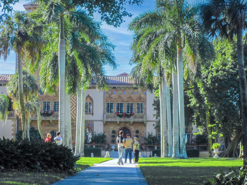 people walking beneath tall palm tree and toward a large house in the Ringling Museum