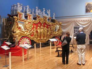 a couple looking at a large red and gold cart in a museum