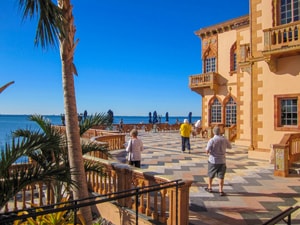 people on a terrace by a large home overlooking a bay