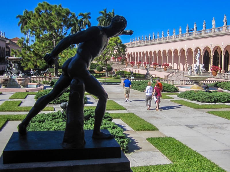 people walking past a large statue in a courtyard