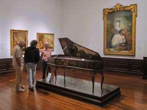 people looking at a harpsichord in a museum