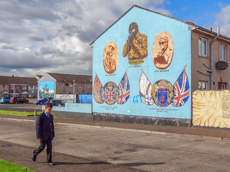 A boy walking past a large wall mural in the Catholic and Protestant neighborhoods. A visit there one of the things to do in Belfast