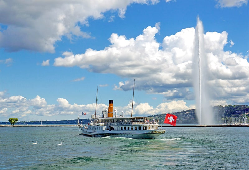 An old lake steamer passing a water jet shooting high awards in Lake Geneva, one of the best places in Switzerland