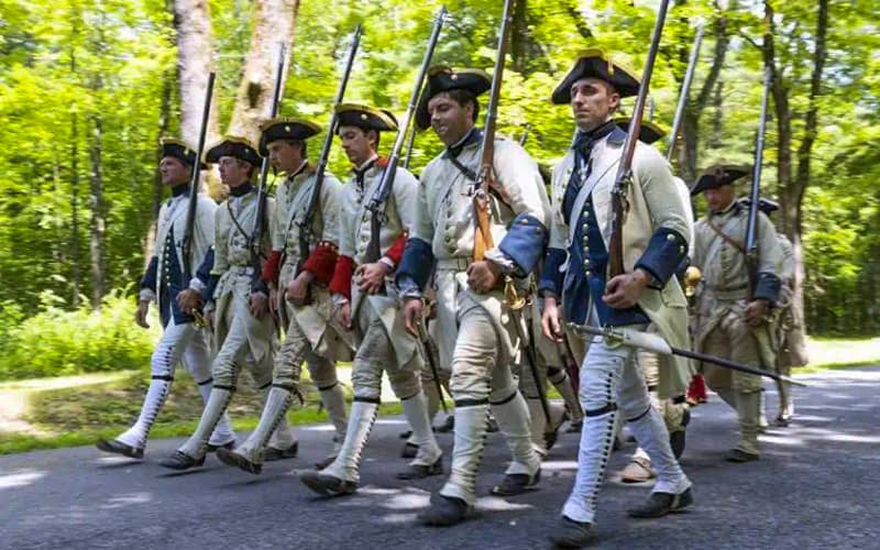 soldier in 18th-cetnurey uniforms marching through the woods