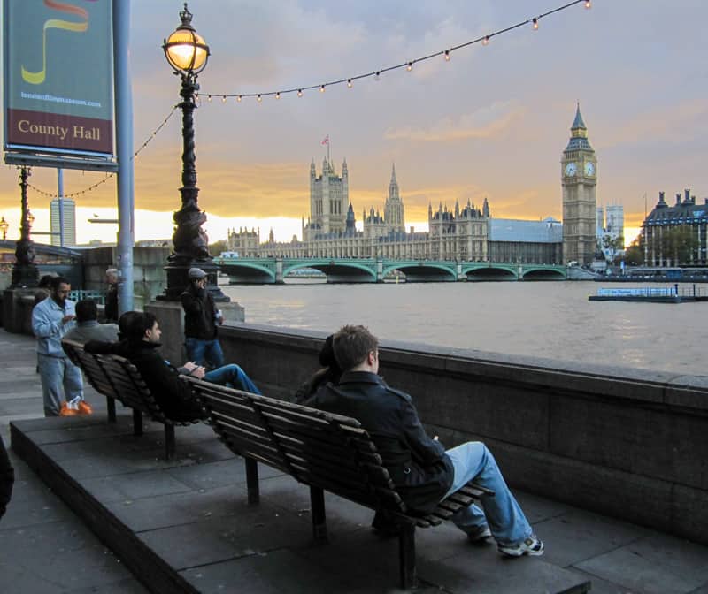 people on benches along the Thames River at sunset
