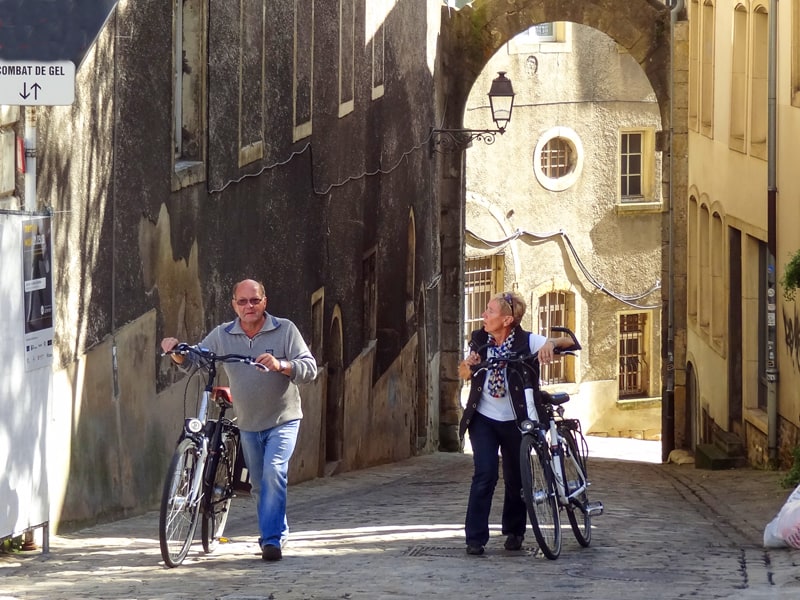 an older couple with bicycles in an old town, one of the things to do in Luxembourg