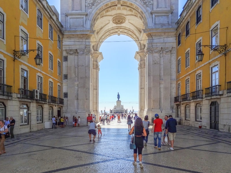 people walking towards a very large arch in Lisbon, one of the best places to visit in Portugal