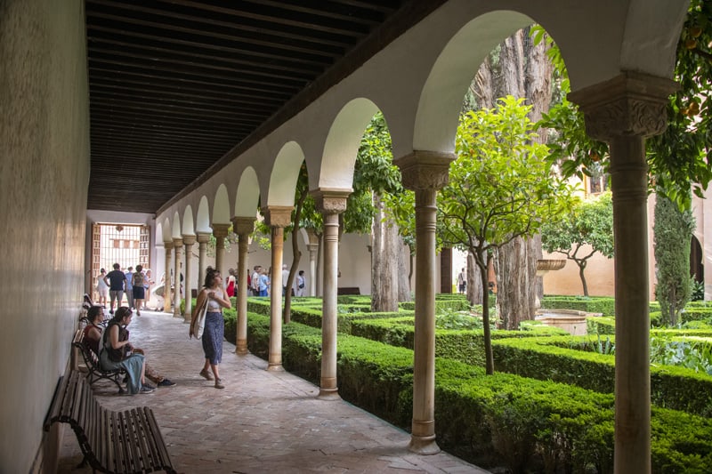 a woman walking along a large patio near a formal garden