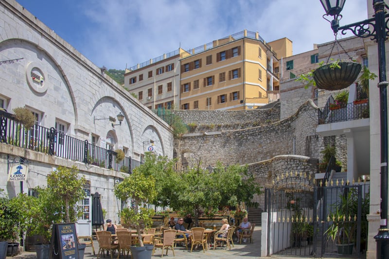 people sitting in an outdoor cafe by high stone walls - one of the things to do in Gibraltar
