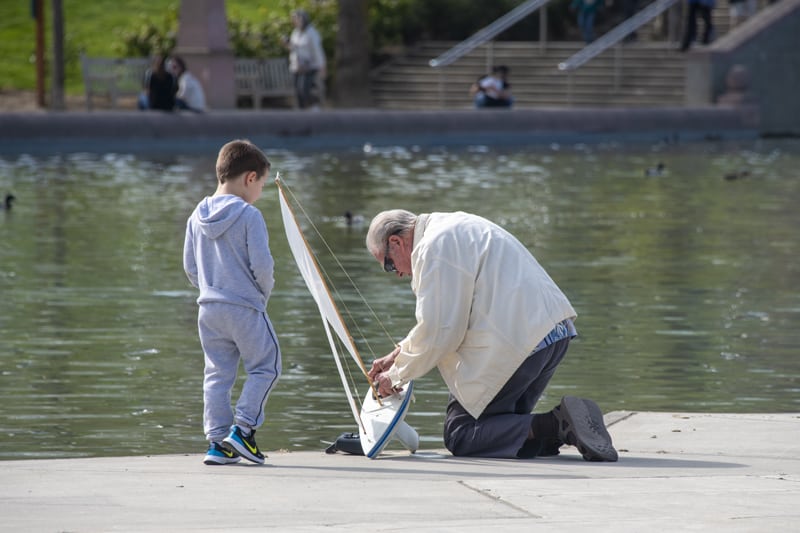 a grandfather and child sailing a toy sailboat on a park pond, one of the things to do in Bellevue