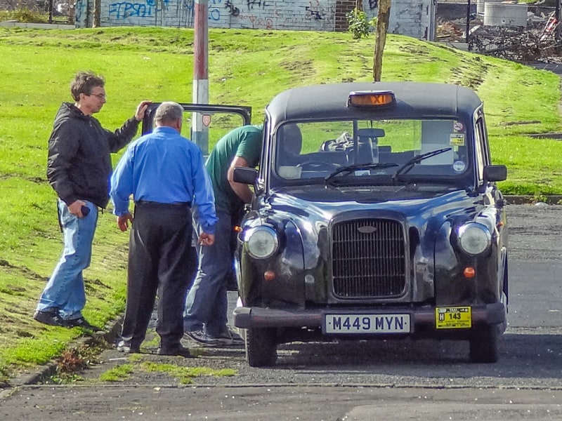 men getting into an old black taxi