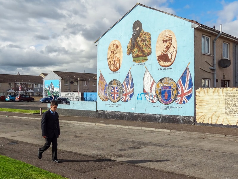 a boy walking past a building that has murals of soldiers painted on its side