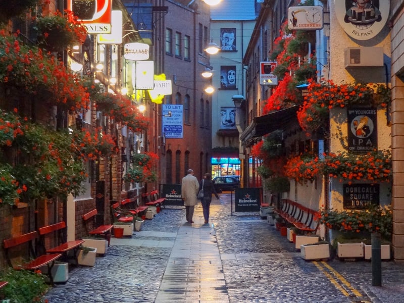 people walking down a street with many flower boxes on windows - seen on a black taxi tour of Belfast