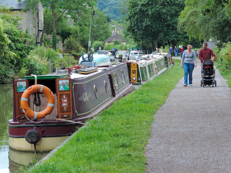 people walking along a path past moored boats