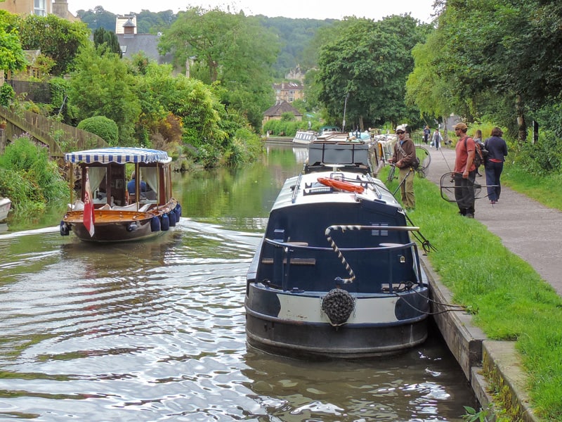 people on a path watching a canal boat go by