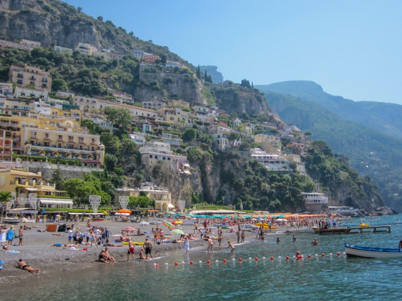 people on a beach with hotels on a steep hillside on the Amalfi Coast - one of the Top 10 Places to Visit in Italy