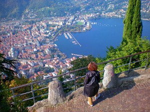 a woman standing on a road looking at a city and lake far below