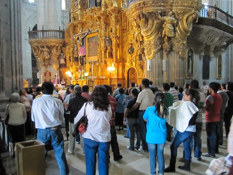 a crowd of people by a golden altar in a large cathedral- one of the places to visit in Mexico City