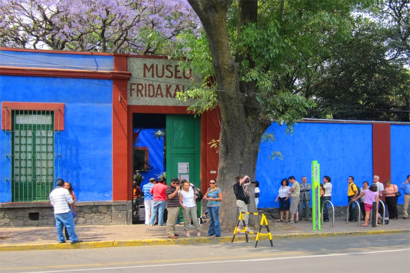 a line of people in front of a blue and red wall at the Frida Kahlo Museum - one of the places to visit in Mexico City