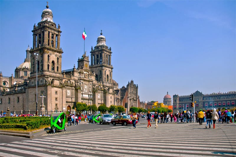 people walking past a large cathedral on a vast square - one of the places to visit in Mexico City