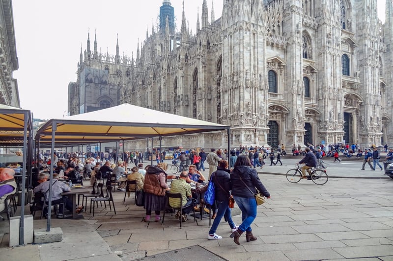 people siting in outdoor cafes near a large ornate cathedral