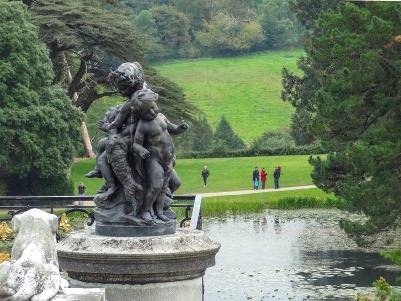 a statue of cherubs by a lake where people are walking in a large garden