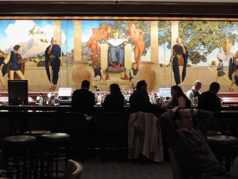 people at a bar which has a beautiful painting on the wall