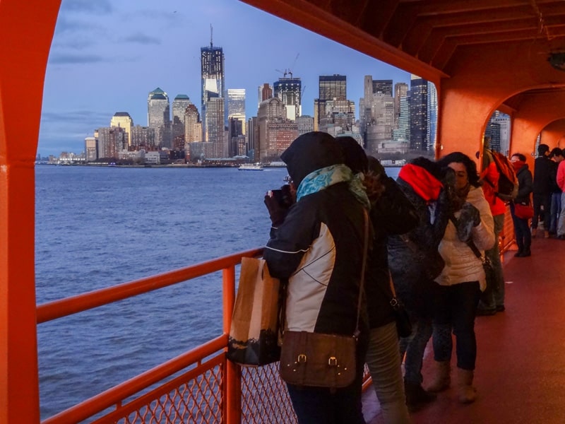 people on the deck of a a ferry looking at the buildings of Manhattan at dusk
