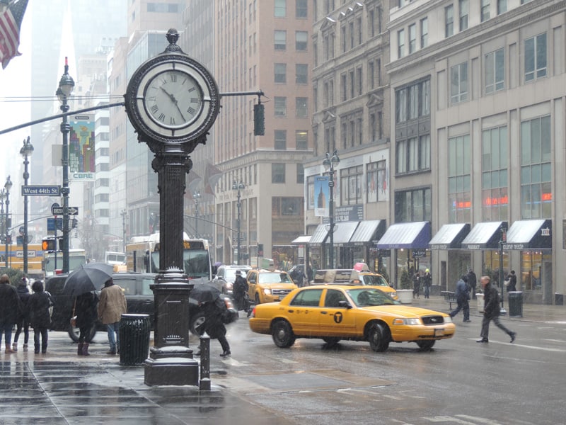 taxis by a large clock on a snowy street in New York in winter
