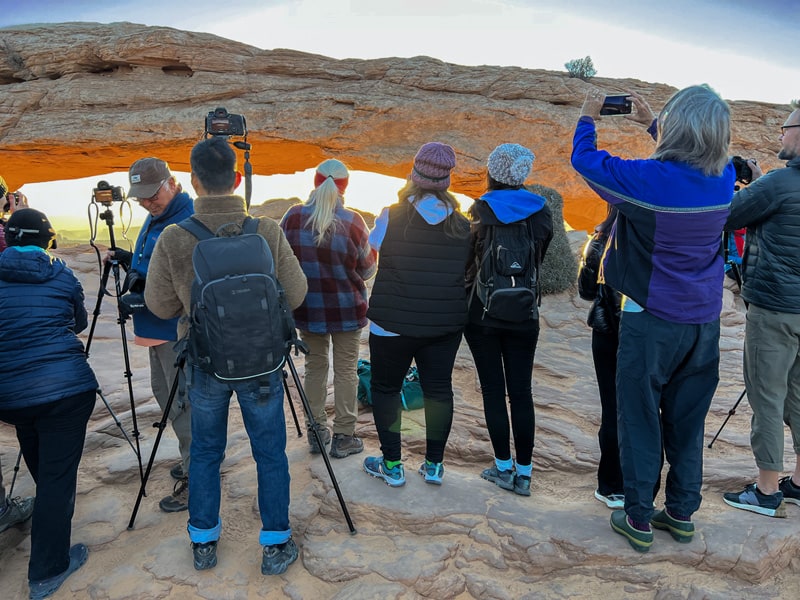 people standing on a large rock at Mesa Arch watching the sunrise