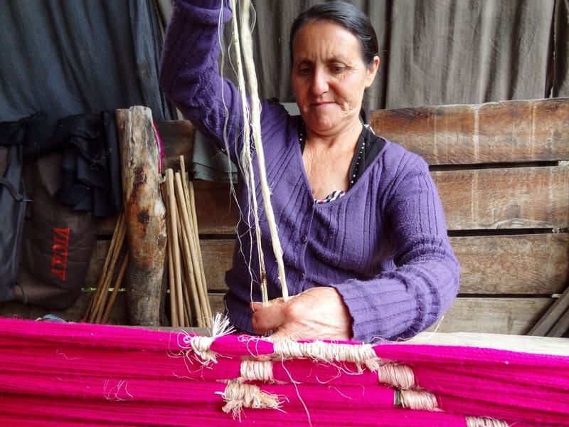 a woman weaving a bright pink fabirc on an old loom