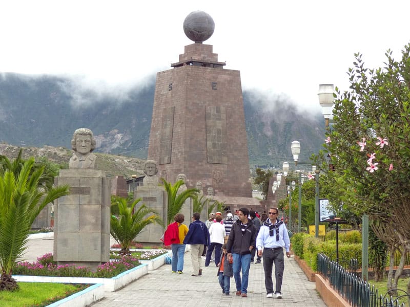 people walking by a tall monument on the equator, one of the top places to visit in Ecuador
