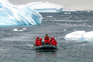 people in red jackets on a raft passing icebergs on an expedition in Antarctica