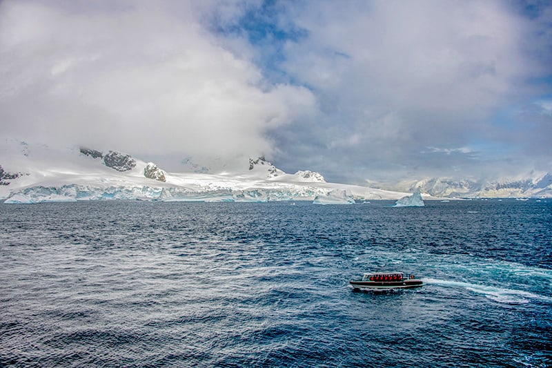 a small boat on the ocean in front snow-covered mountans