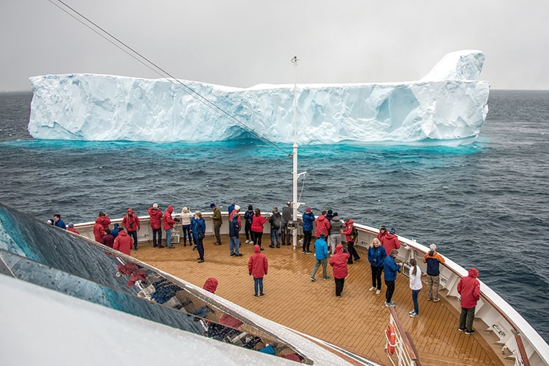 people on a ship looking at a large blue iceberg on an expedition in Antarctica