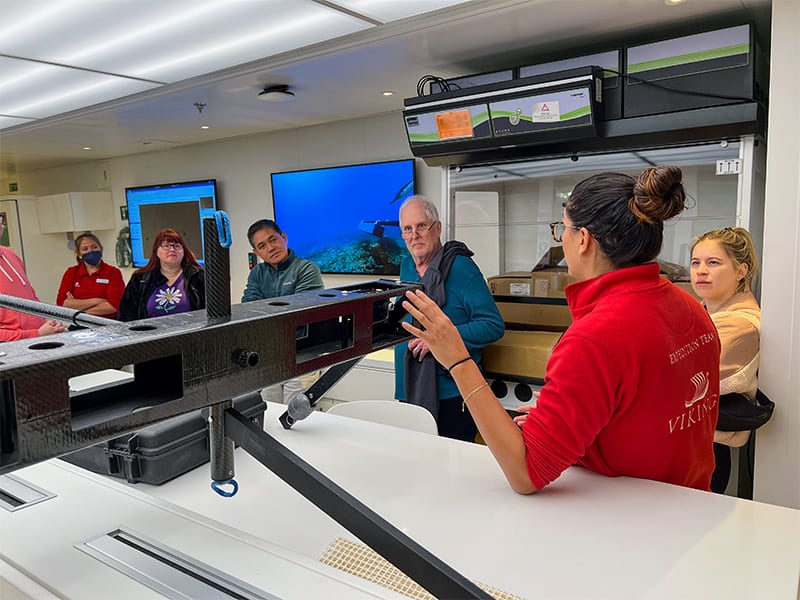 a woman in a red shirt speaking with a group of people in a laboratory 