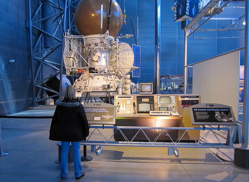 a woman looking at a desk with monitors by a solar system probe