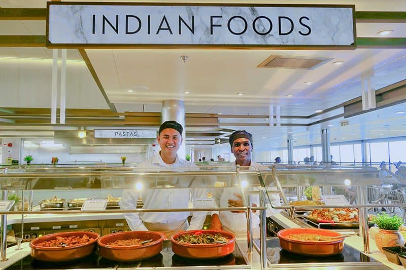 two men in a ship's dining area under a sign for indian food