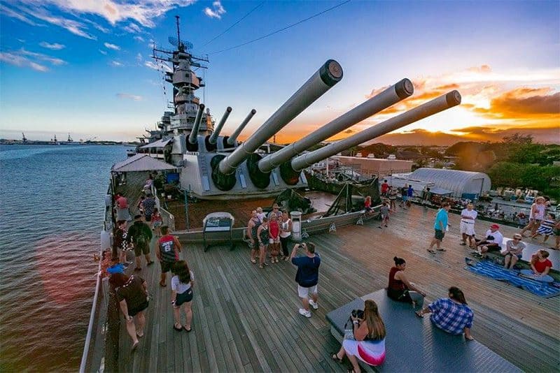 people standing below the gun turrets on a museum ship