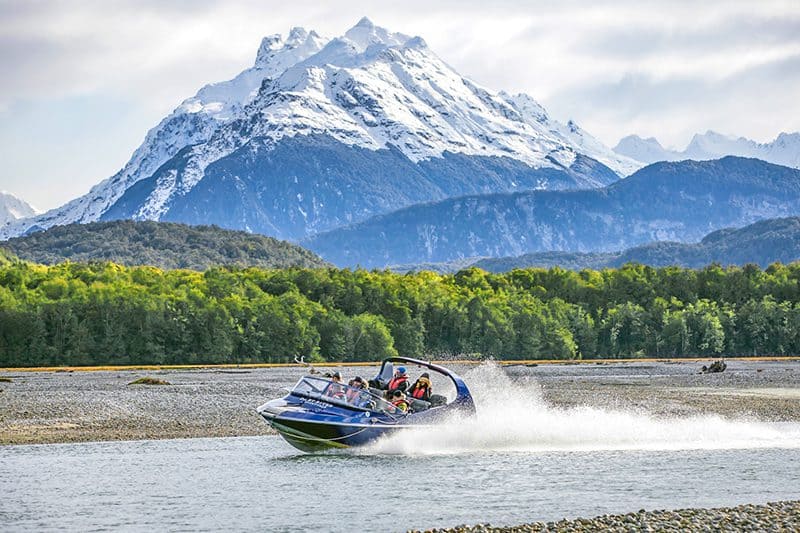 people on a jet boat on a river in front of a mountain – one of the tours in New Zealand