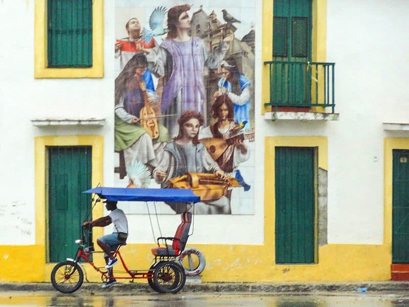 man on bicycle passing a wall mural in Havana