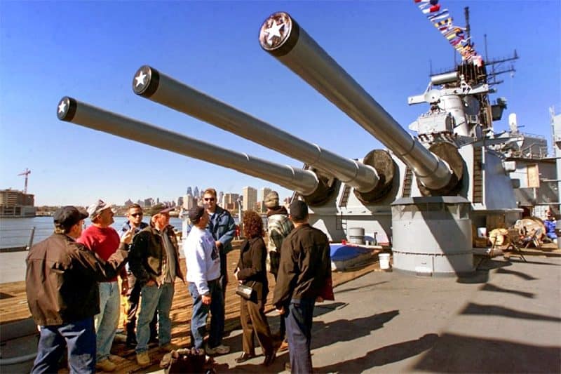 people standing below a gun turret on a battleship