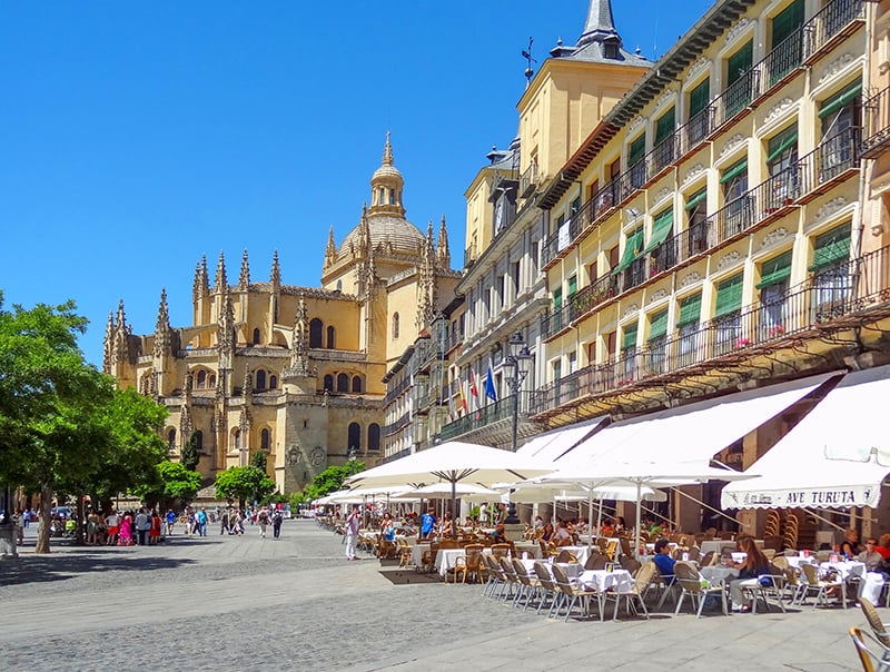 people dining in a large plaza with a cathedral in the distance