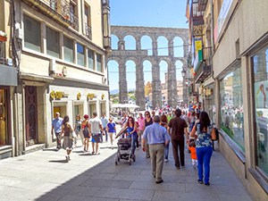 people walking along a street in Segovia with an aqueduct in the distance