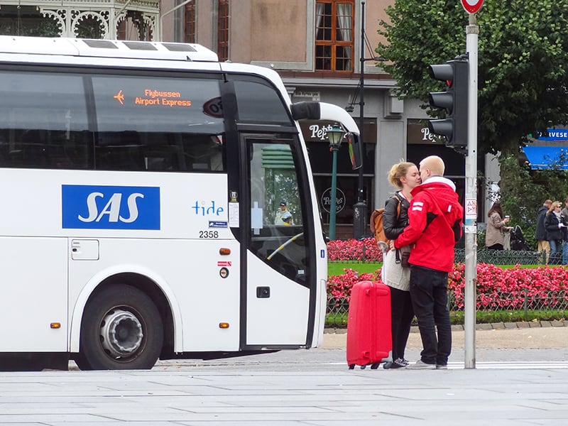 a couple standing and kissing by the Bergeb airport bus