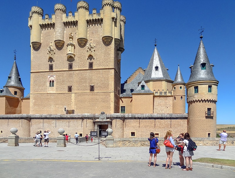 People looking at the turrets of an ancient castle in Segovia