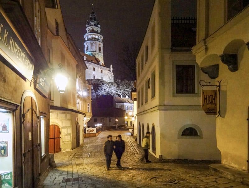 a couple walking down a street below a castle at night in the low season in Europe